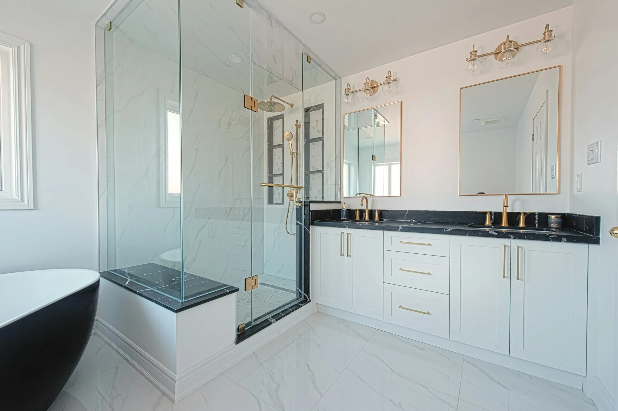 Bathroom with a glass-enclosed shower, a black stone bench and a double vanity with brass fixtures