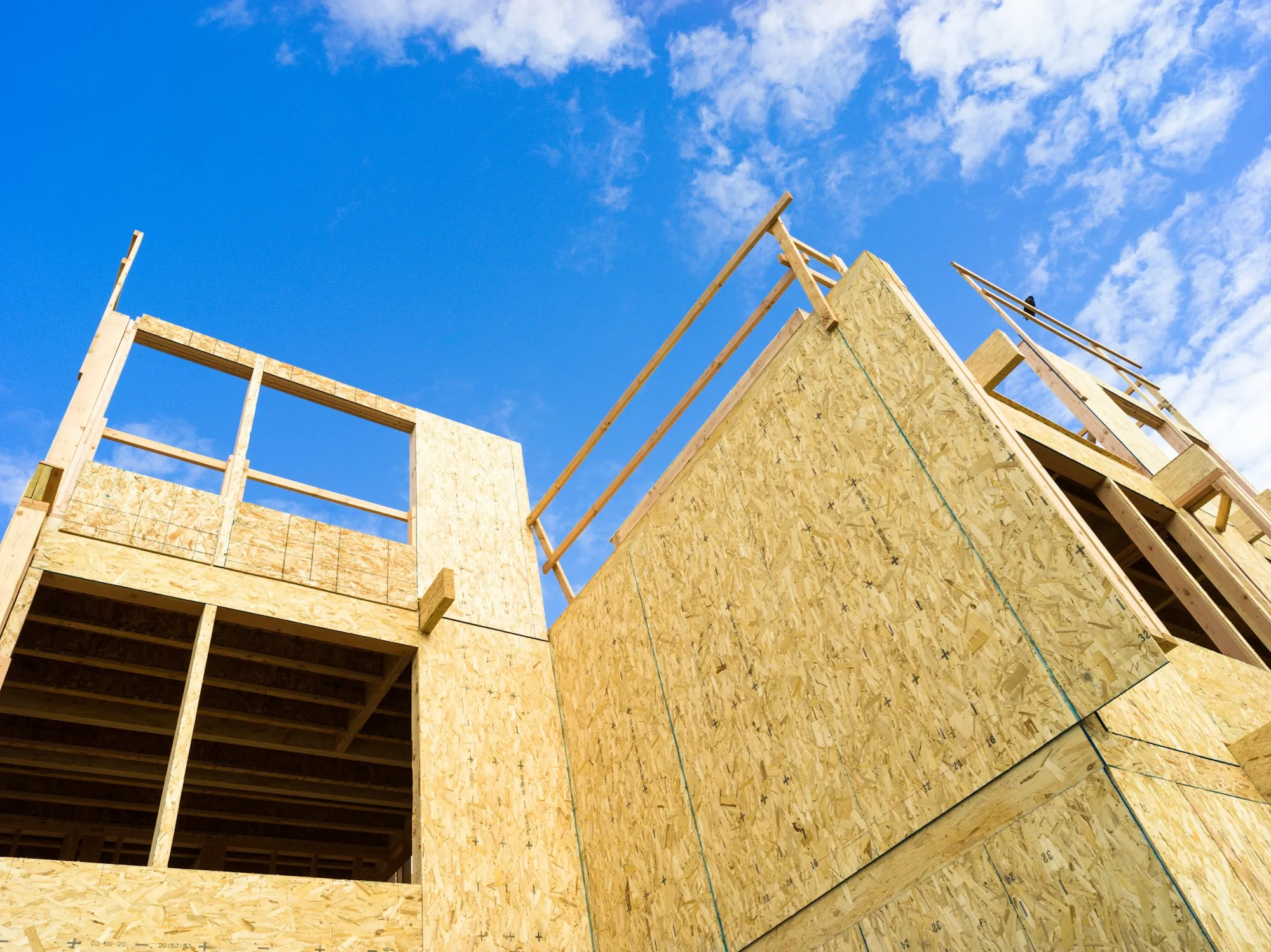 Two-story addition framed and sheathed in plywood against a blue sky