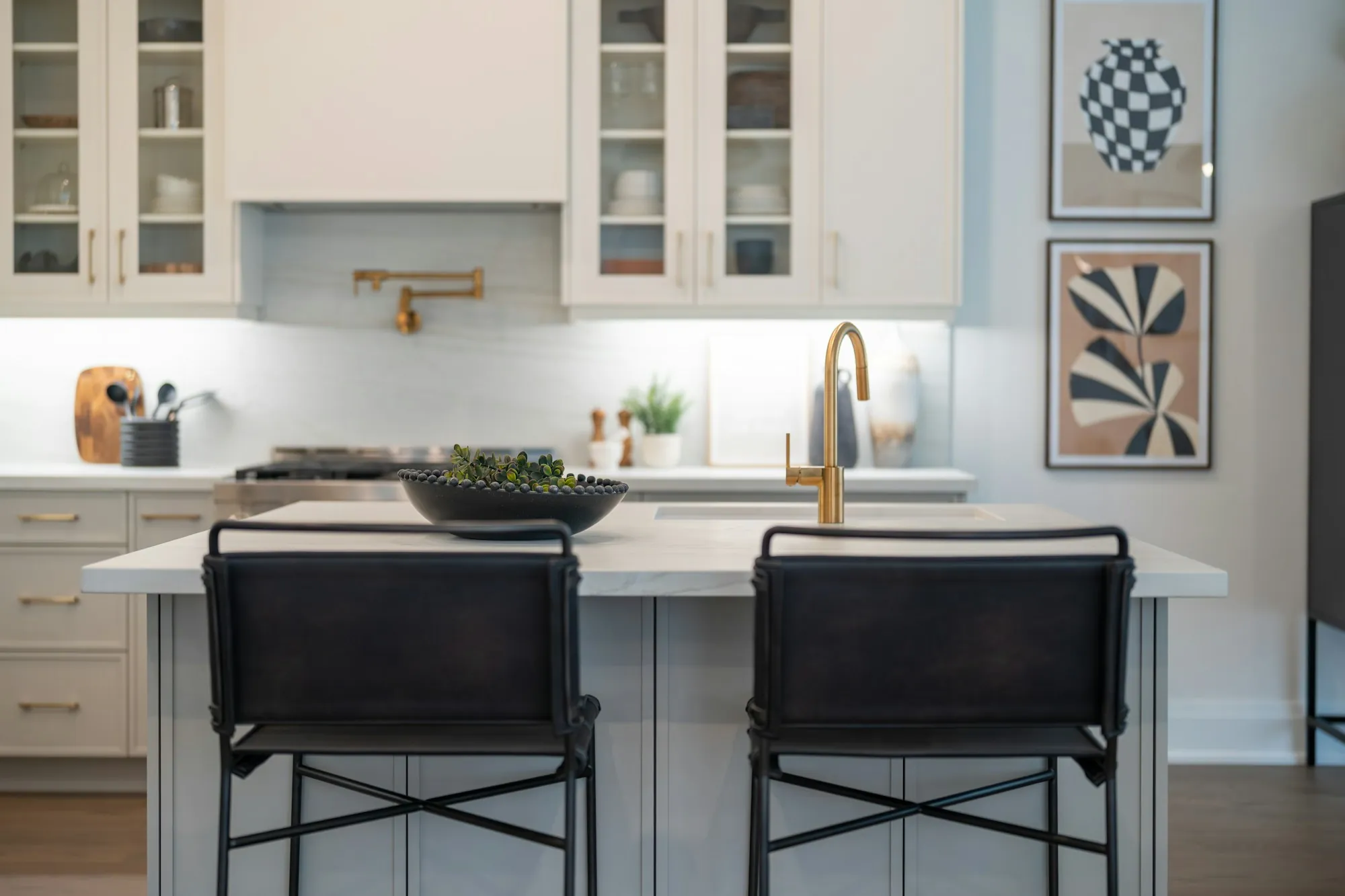 Kitchen island with black leather stools, white cabinets and a brass faucet